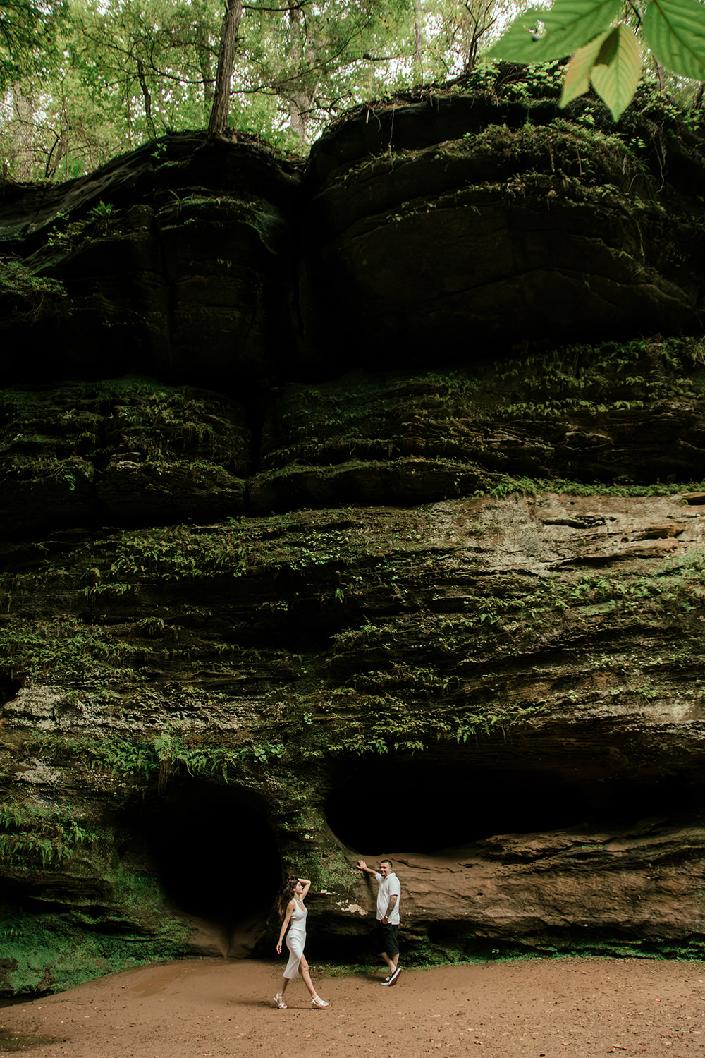 Full-length shot of a couple wearing neutral outfits popping against the deep green forest setting.