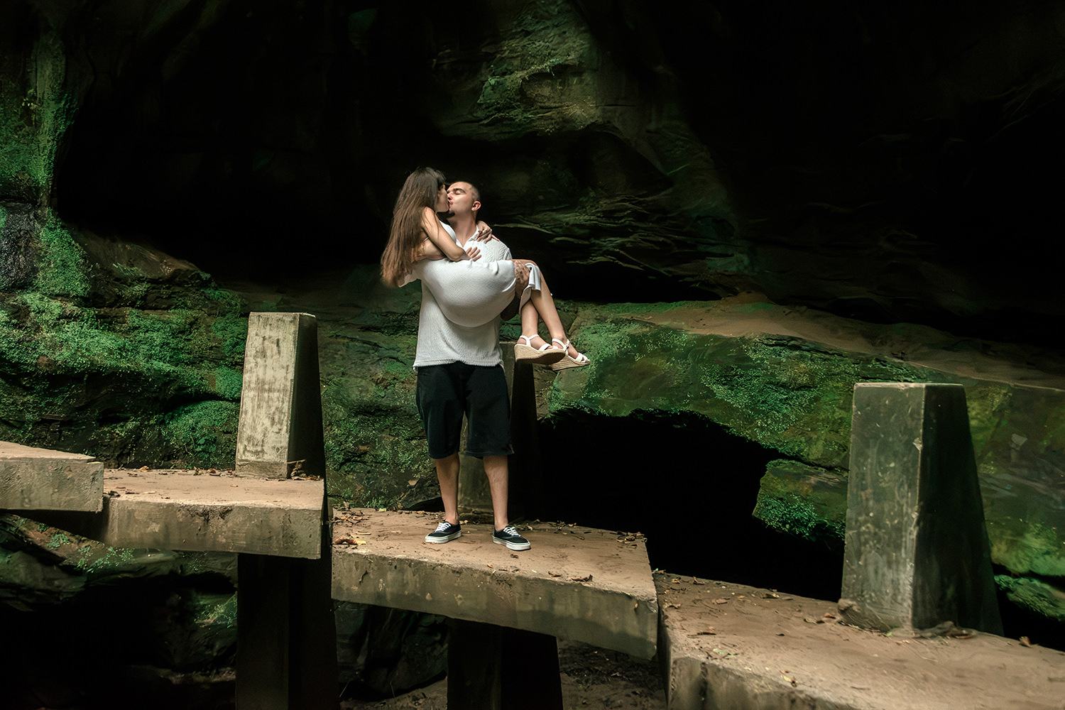 Low-angle view of the couple holding hands under the high arching sandstone walls of Old Man’s Cave.