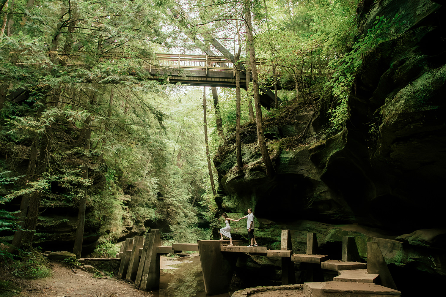 Wide shot of a couple standing beside the rocky creek bed inside the shaded Old Man’s Cave gorge.