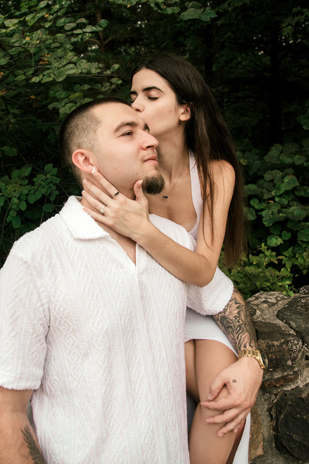 A woman sits on a stone wall at Old Man's Cave and kisses her fiancé on the forehead. The man's hand is on her knee.