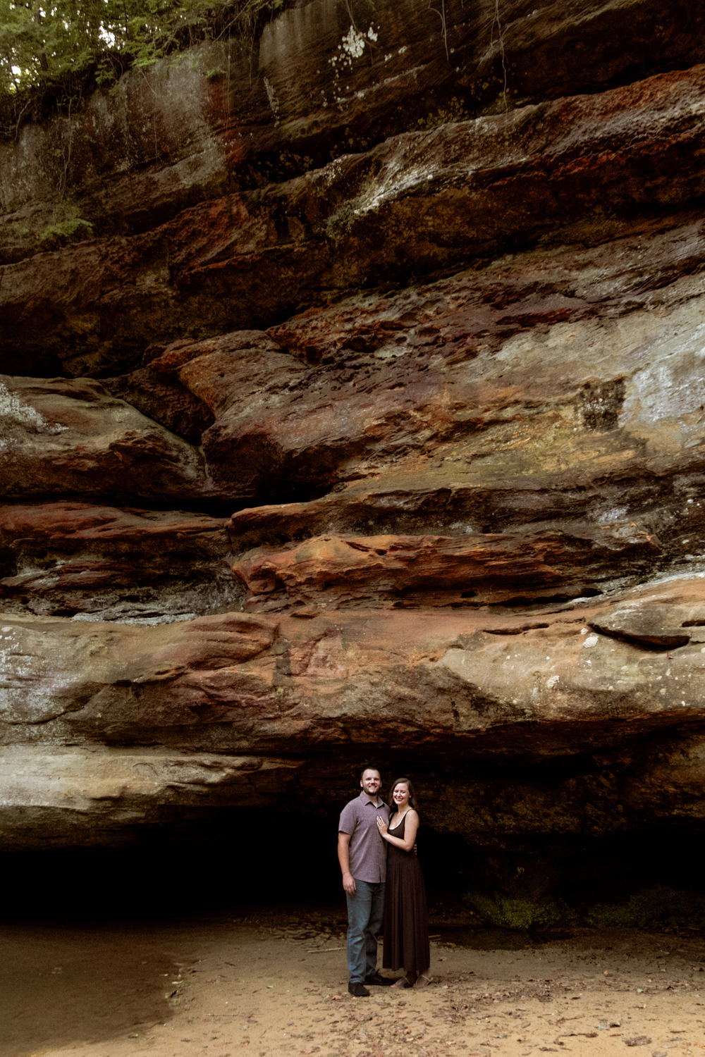 Wide angle shot of a couple dwarfed by the massive, ancient sandstone cliffs of Hocking Hills.