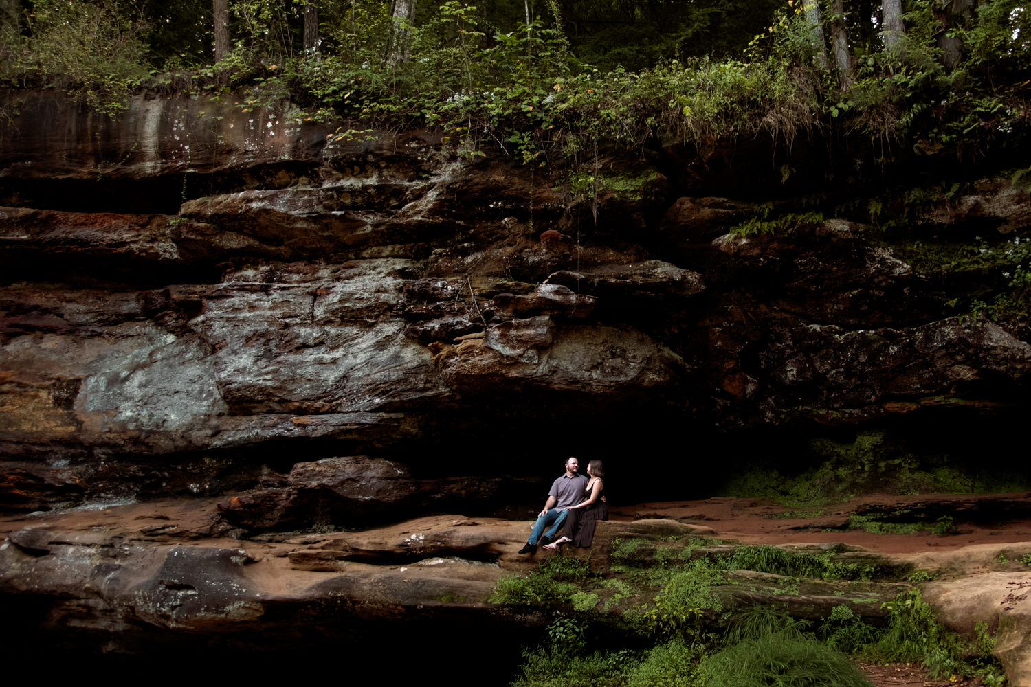 Couple sharing a quiet moment on a rock ledge surrounded by vibrant green ferns and gorge hemlocks.