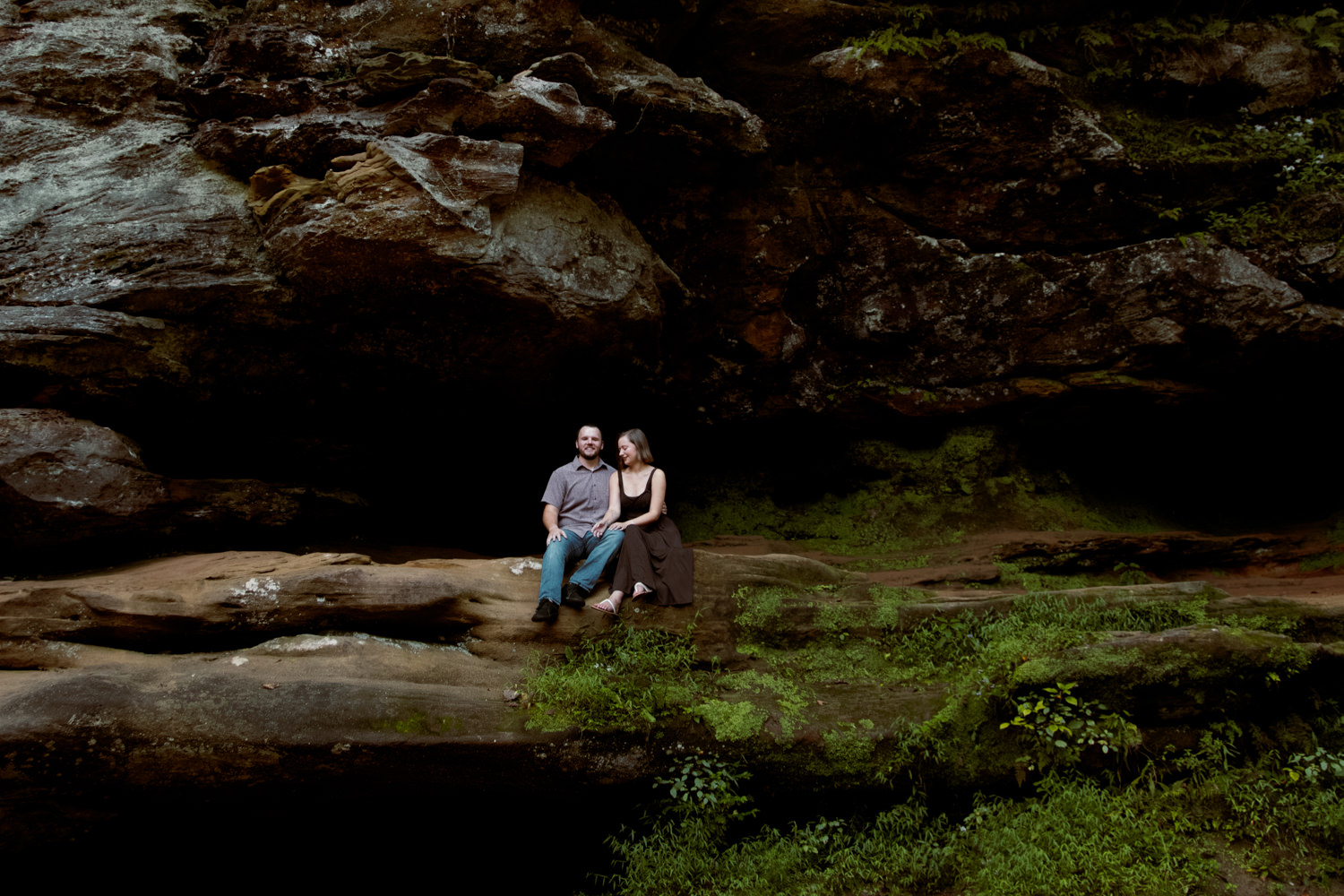 Couple sharing a quiet moment on a rock ledge surrounded by vibrant green ferns and gorge hemlocks.