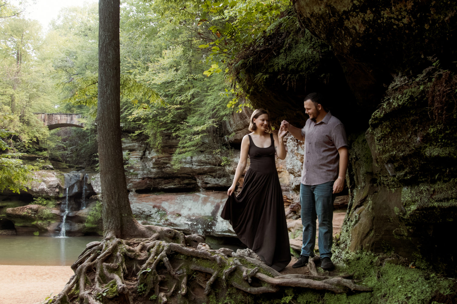 Close-up of a married couple smiling and holding hands near the mossy sandstone cliffs at Upper Falls.