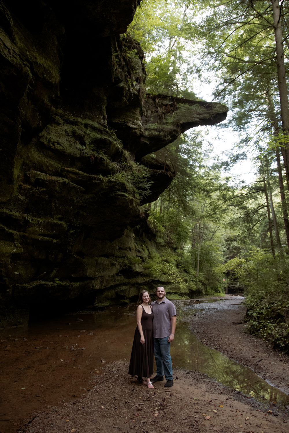 Classic portrait of a couple posing beneath a giant sandstone rock overhang in the forest.