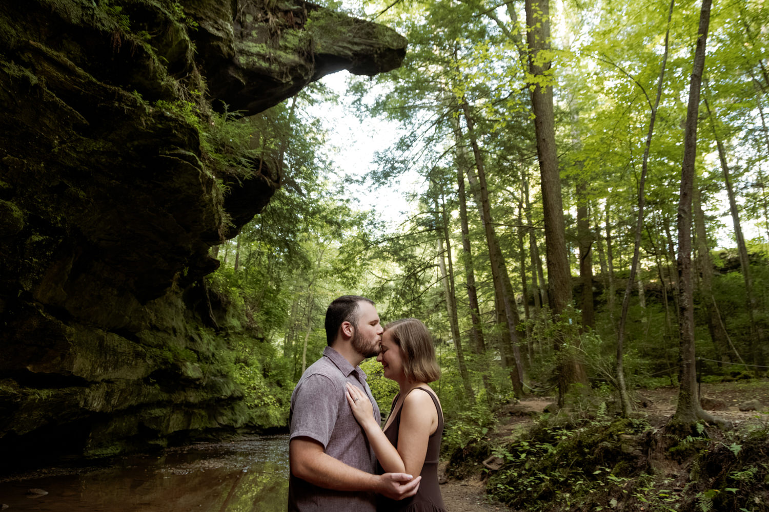 Romantic portrait of a couple kissing beneath a giant sandstone rock overhang in the forest.