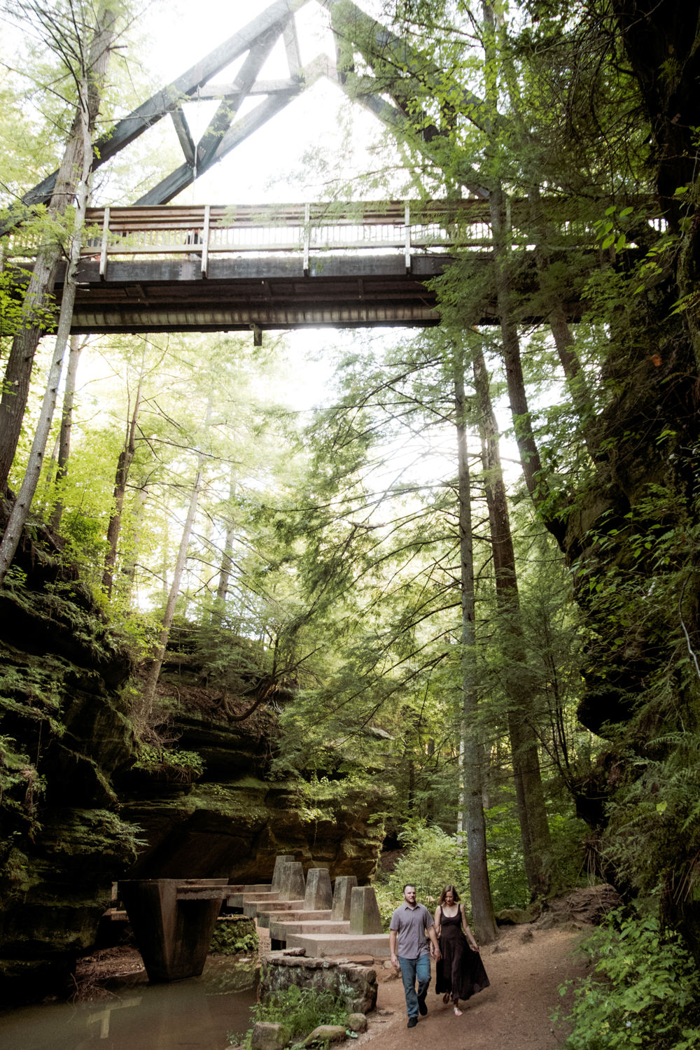 Dramatic view looking up at the high rock faces, hemlock treetops, and an a-frame bridge in Hocking Hills.