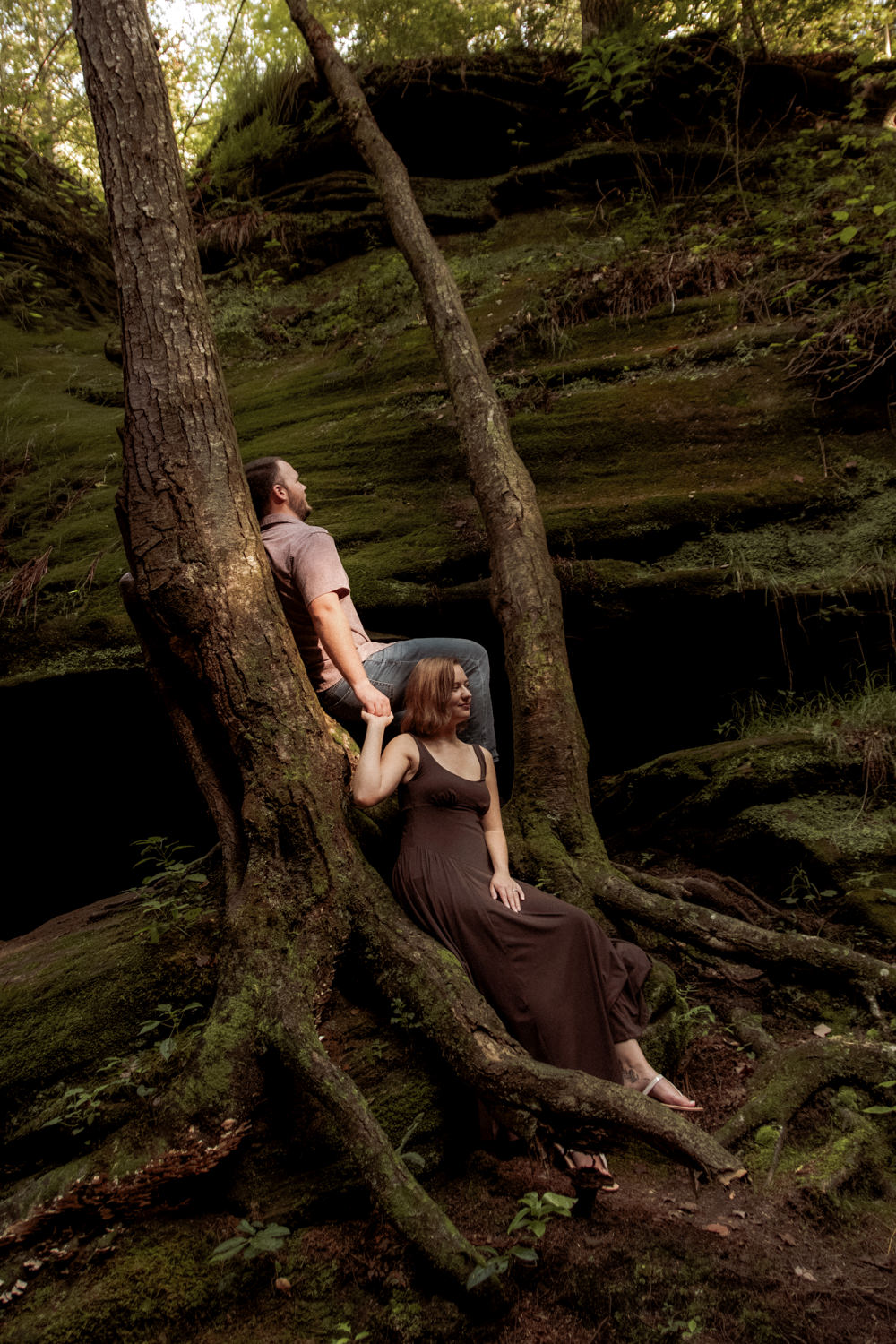 Couple sharing a quiet moment on tree roots surrounded by vibrant green ferns and gorge hemlocks.