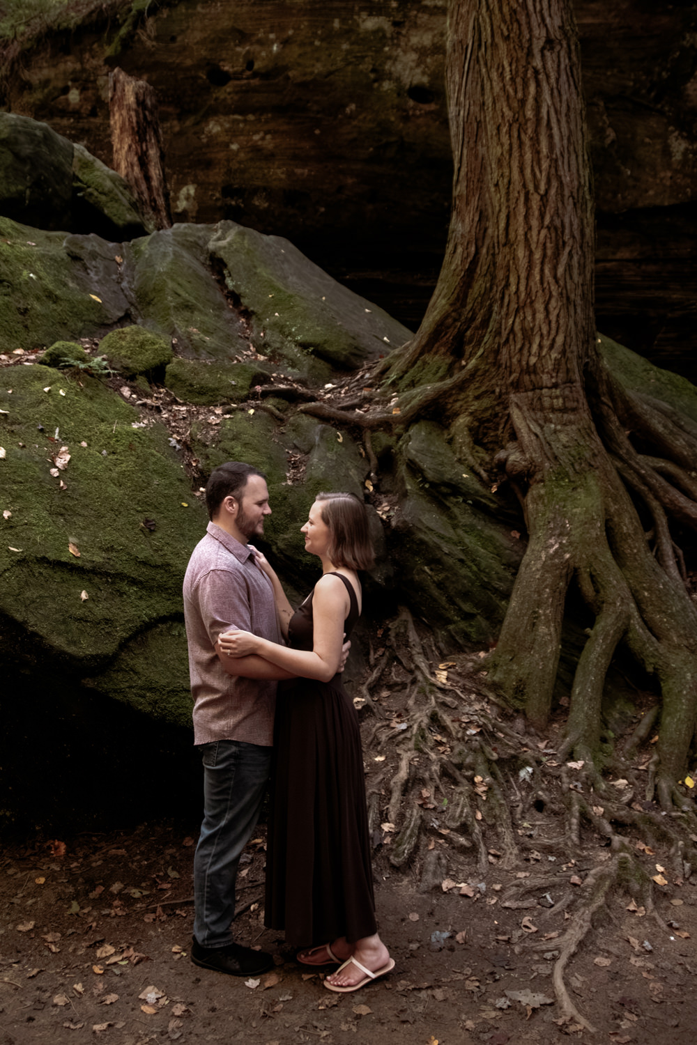 Couple standing together at the base of ancient tree roots in Hocking Hills, Ohio.