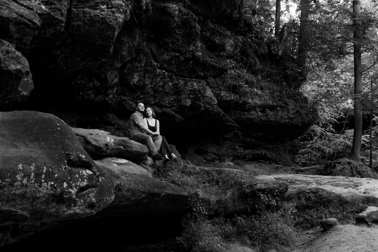 Black and white wide portrait of a couple sitting on a cliffside overlook in Hocking Hills.
