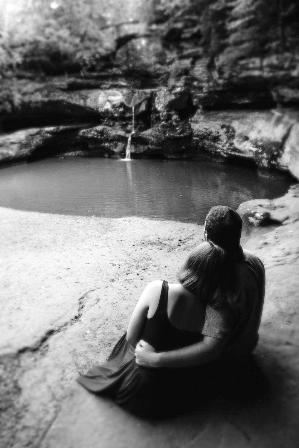 Black and white photograph of a couple sitting together on a rock wall overlooking a waterfall.